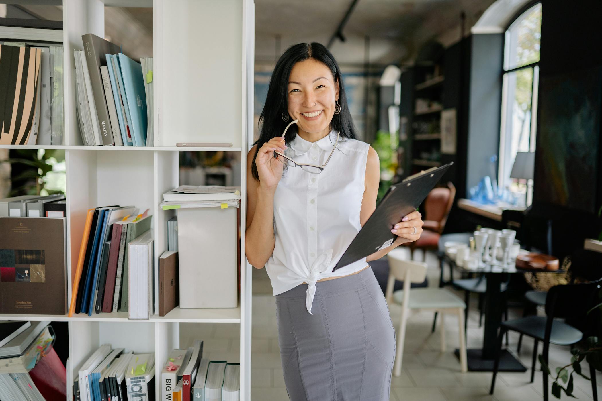 Our clients save thousands on annual agency fees. No Contract. Proven Results. Don't Out-spend your competition, Out-think them! Amplify Your Business Growth With Expert Digital Marketing That Actually Works.. Smiling woman holding eyeglasses and clipboard in a contemporary office.